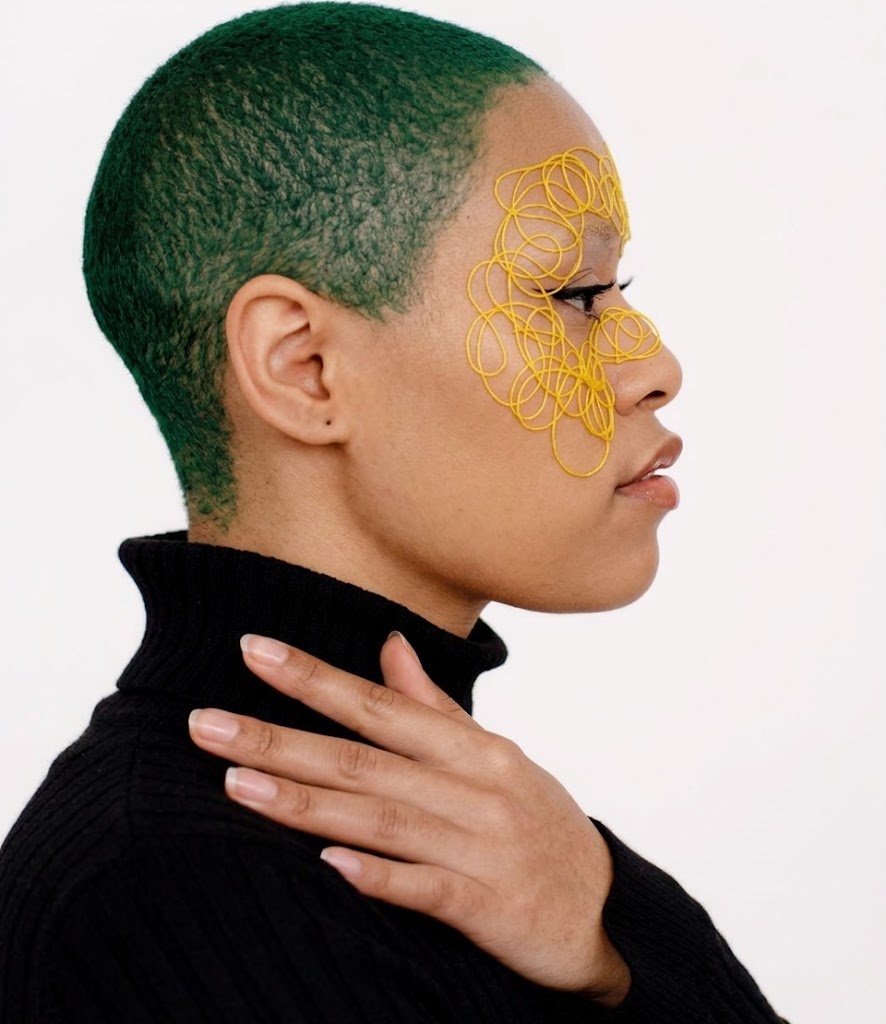 Jamaican woman with green hair and yellow face art looking right